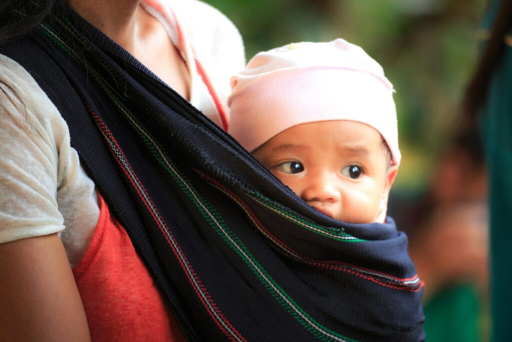 Mother carrying her baby in a sling, showcasing a tender moment of parenthood.