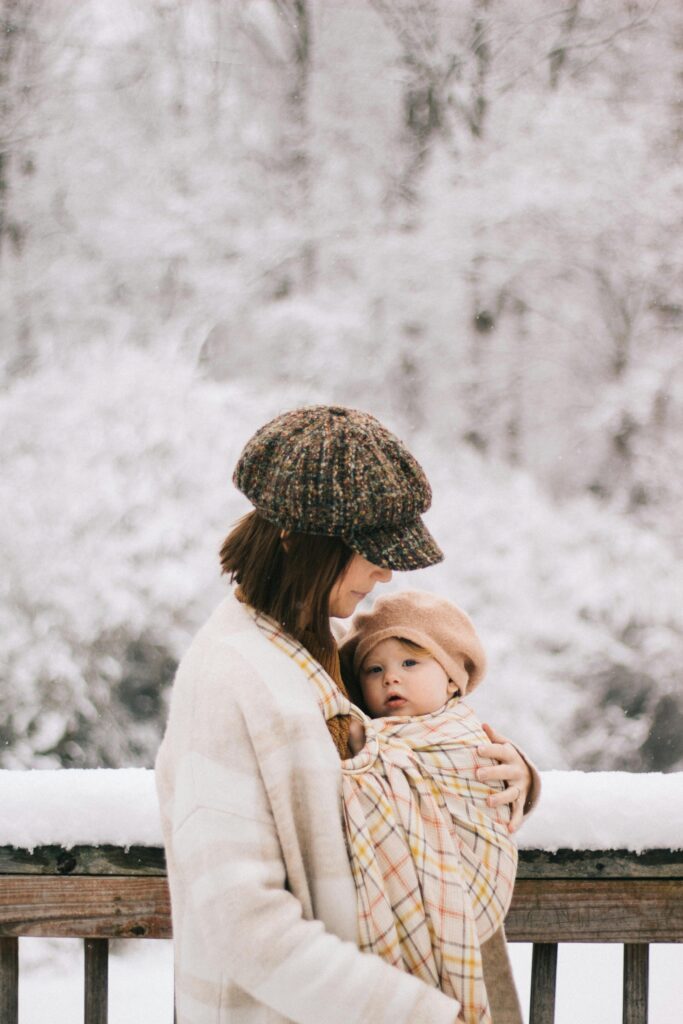 Mother cradling baby in a sling amidst a serene snowy backdrop, showcasing gentle connection.